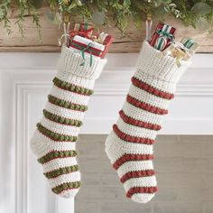 two christmas stockings hanging from a mantel decorated with green, red and white ribbon