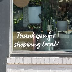 a sign that says thank you for shopping local in front of a window with potted plants