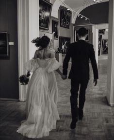 the bride and groom are walking down the hall together in black and white, holding hands