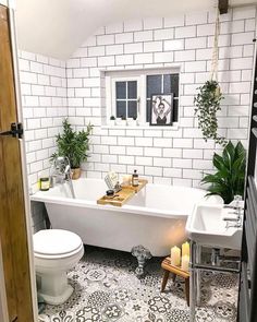 a white bath tub sitting next to a toilet in a bathroom under a window with potted plants