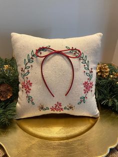 a white pillow with a red ribbon on it and some pine branches in the background