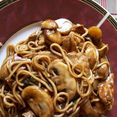 a plate full of noodles and mushrooms on a table cloth with chopsticks in it