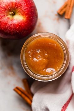 an apple and cinnamon butter in a jar on a towel next to some cinnamon sticks