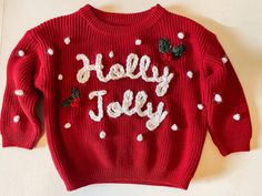 a red sweater with white polka dots and the words holly jolly written on it is laying on a table