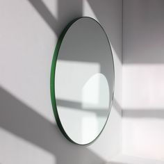 a round mirror mounted to the side of a white wall next to a green shelf