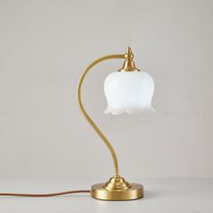 a lamp that is sitting on top of a white tablecloth with a gold base