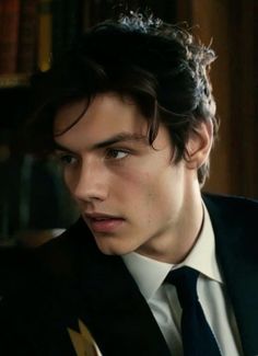 a young man wearing a suit and tie in front of a bookshelf filled with books