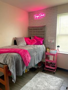 a bed room with a neatly made bed and a pink neon sign on the wall