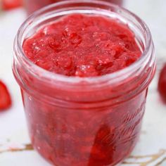 a jar filled with strawberry jam sitting on top of a white table next to strawberries