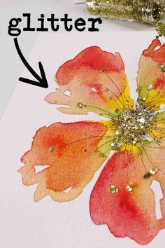 a piece of paper that has been painted with gold glitter and is next to a flower