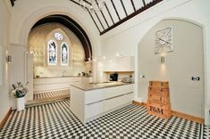 a kitchen with black and white checkered flooring next to an arched window at the end of the room