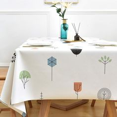 a white table cloth with trees and flowers on it in front of a blue vase