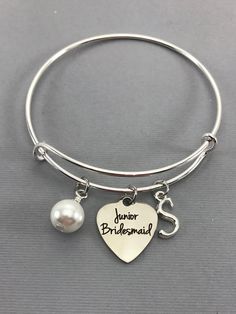 Junior Bridesmaid charm bangle bracelet with a pearl charm and initial. Features: Adjustable Bangle Bracelet, Silver Plated Measures 61mm . Measurements: 18mm x 15mm Junior Bridesmaid charm is made of stainless steel Measurements: 19mm x 22mm Each purchase will arrive packaged in a cute kraft gift box ready to give as a present or a fun gift for yourself! Add on a birthstone charm for $3.00 Additional add on charms or initial charms $3.00 https://www.etsy.com/shop/OurLittleCharms?ref=hdr_shop_me Junior Bridesmaid Proposal, Bride Gift Ideas, Pearl Wedding Jewelry, Proposal Wedding, Adjustable Bangle Bracelet, Pearl Jewelry Wedding, Wedding Party Gift, Adjustable Bangle, Bangle Bracelets With Charms