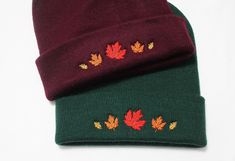 two beanies with autumn leaves on them sitting next to each other in front of a white background