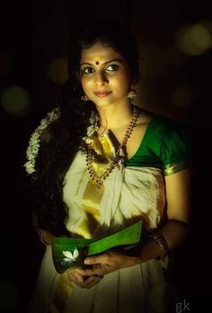 a woman in a green and white sari holding a vase with flowers on it