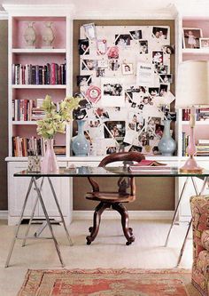 a desk with a chair, vases and pictures on the wall behind it in front of a bookshelf