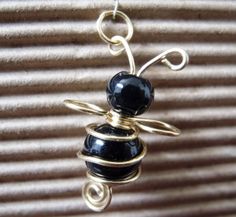 a black bead and gold wire necklace with a bee charm hanging from it's side