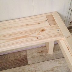 a wooden bench sitting on top of a hard wood floor next to a white wall