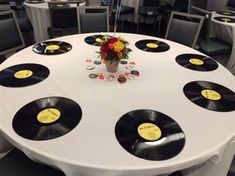 a white table topped with lots of black and yellow vinyl record records next to a vase filled with flowers