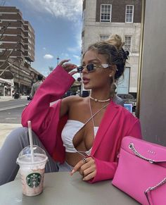 a woman sitting at a table with a pink purse and starbucks drink in front of her