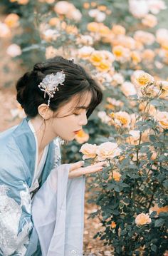 a woman in a blue kimono is smelling some yellow and white flowers with her hands