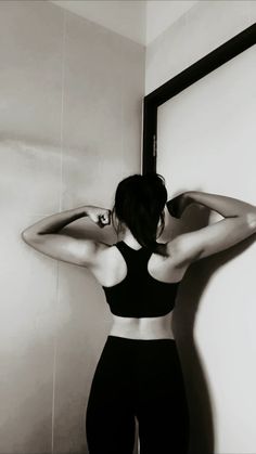 a woman standing in front of a mirror with her back to the camera and arms behind her head