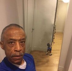 an older man taking a selfie in front of a mirror with a little boy behind him