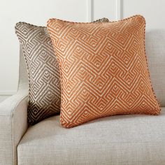 two orange and brown pillows sitting on top of a white couch next to each other