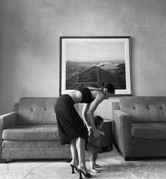 a woman bending over to pick up a child's shoe from the floor in front of a couch