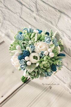 a bridal bouquet with blue, white and green flowers on it's side