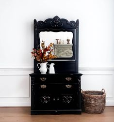 a black dresser with mirror and vases on it next to a wicker basket