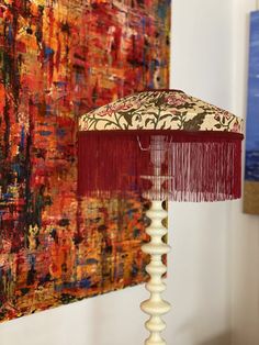 a lamp with a red shade on it in front of a colorful painting and artwork