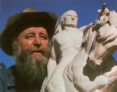 a man with a beard standing next to a statue