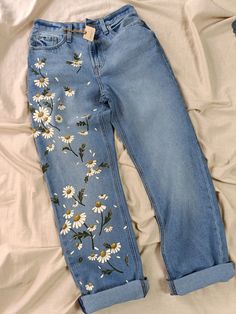 a pair of jeans with daisies embroidered on the side, laying on a bed