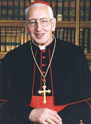 an older man in a priest's outfit standing in front of bookshelves