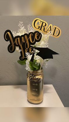 a graduation cake topper in a mason jar with white flowers and greenery on the table