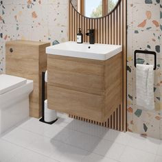 a white toilet sitting next to a bathroom sink under a round mirror on a wall