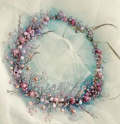 a wreath made out of pink flowers and pearls on a white cloth covered tablecloth