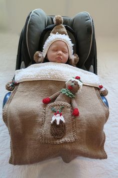 a baby in a car seat wearing a knitted christmas hat and blanket with pom poms