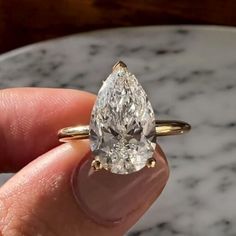 a close up of a person's hand holding a ring with a pear shaped diamond