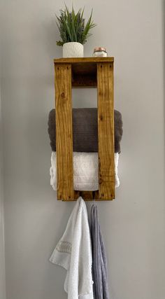 a wooden shelf with towels hanging from it's sides and a potted plant on top