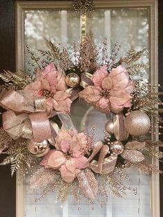 a wreath with pink flowers and gold ornaments hanging on a window sill in front of a glass door