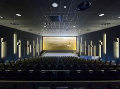 an empty theater with rows of seats facing the stage and projection screen on the wall