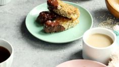 two donuts are sitting on a plate next to some coffee cups and saucers