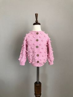 a pink knitted sweater on a mannequin stand with a wooden dummy behind it