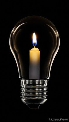 a lit candle in a light bulb on a black background with the reflection of it