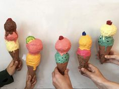 five people holding ice cream cones with different toppings on them in front of a white wall