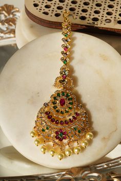 Enhance your traditional allure with the 'Jirisa - Gold AD Maang Tikka.' This exquisite piece, measuring approximately 5.51 inches in height and 1.77 inches in width, is available in two stunning options: Gold and Green, and Gold and Ruby-Green, each adding a touch of elegance to complement your style. The Gold and Green variant delicately features small teardrop-shaped stones dangling from the base, offering a subtle yet captivating charm to your appearance. Alternatively, the Gold and Ruby-Gre Ear Chain, Accessories Ear, Chandbali Earrings, Maang Tikka, Choker Necklace Set, Gold And Green, Traditional Look, Jhumka Earrings, Artisan Craft