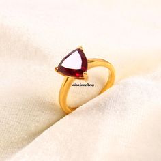 a gold ring with a red stone in the middle on a white cloth background,