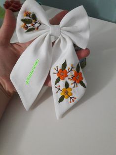 two white bows with orange and yellow flowers on them are being held by someone's hand